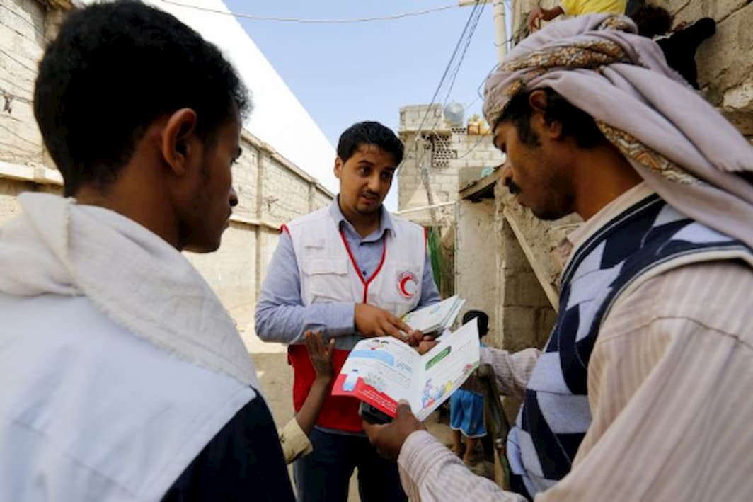 A Red Cross volunteer worker distributes leaflets about cholera to two men on the street.