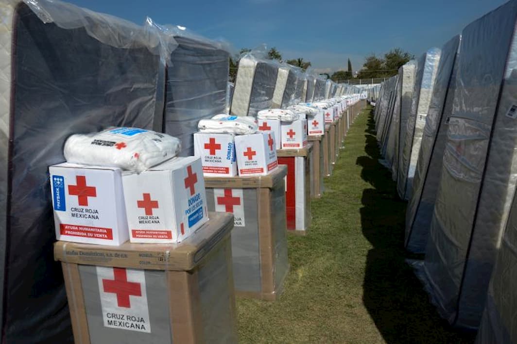 A long row of Red Cross relief packages and boxes set up outside tents in a refugee camp in Mexico.